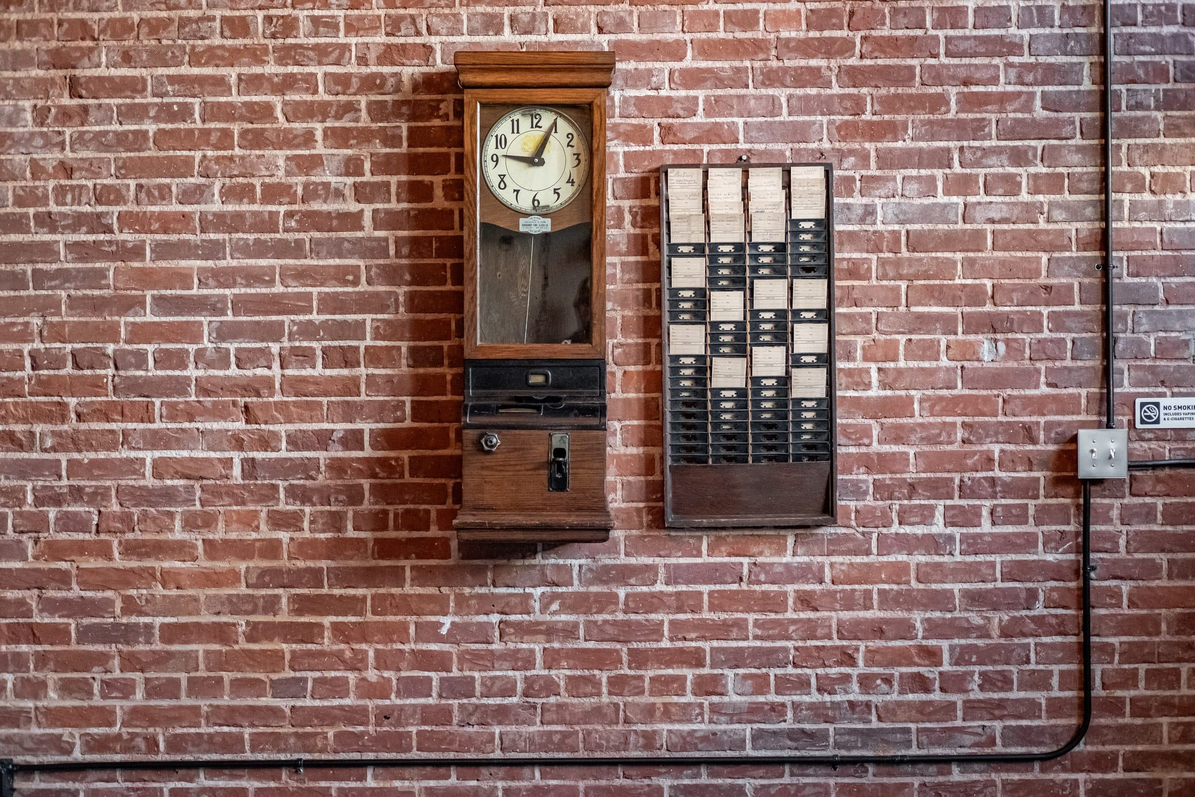 Antique time clock and punch-card rack on the hall's red brick wall