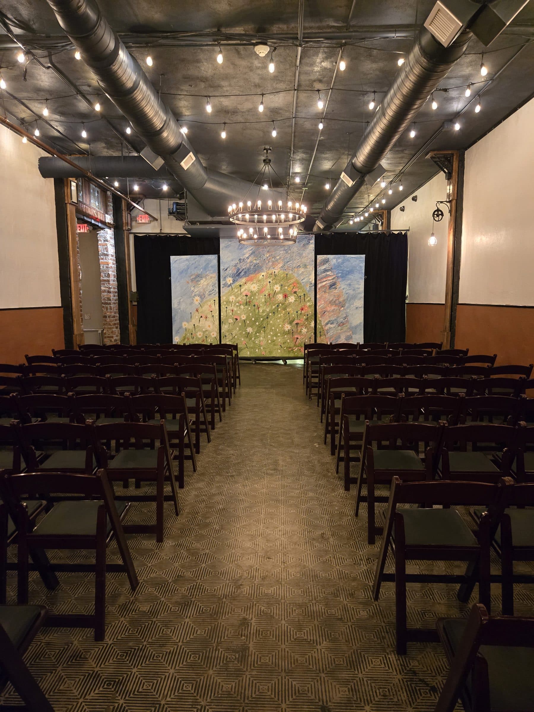 Rows of ceremony chairs leading to an artwork backdrop under chandeliers