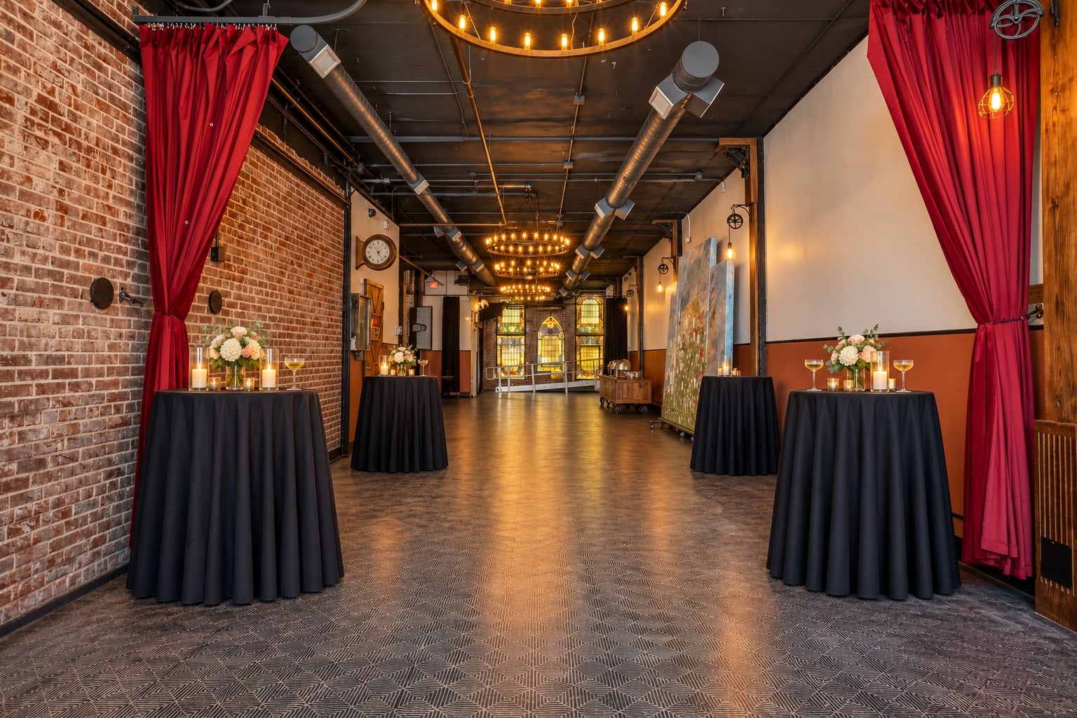 Cocktail tables styled with flowers and candle hurricanes between the hall’s garnet curtains